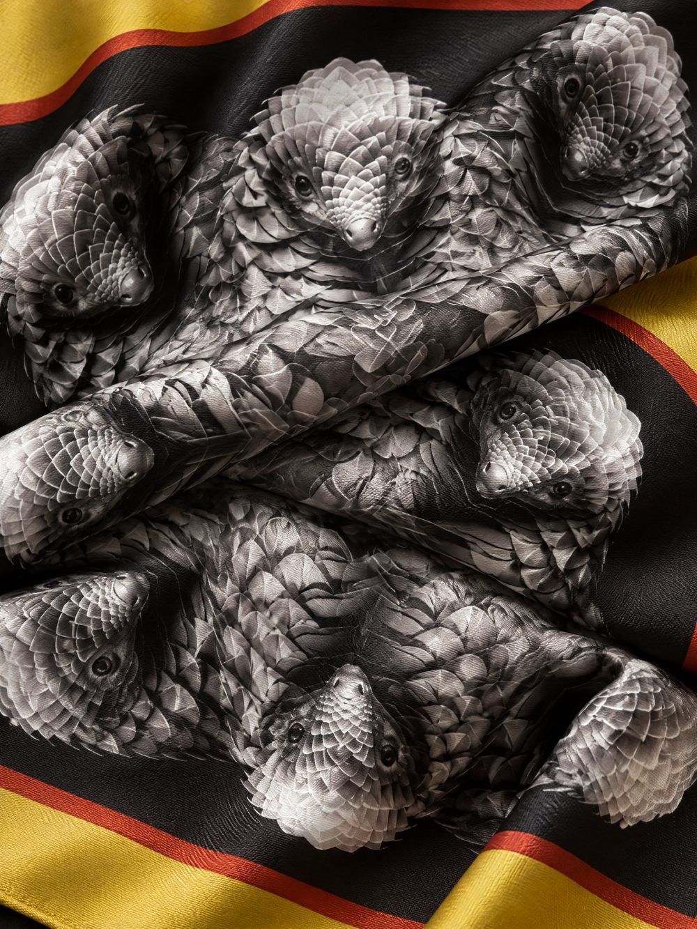 Close-up of The Pangolin's Defence printed on folded fabric in black, silver grey and gold