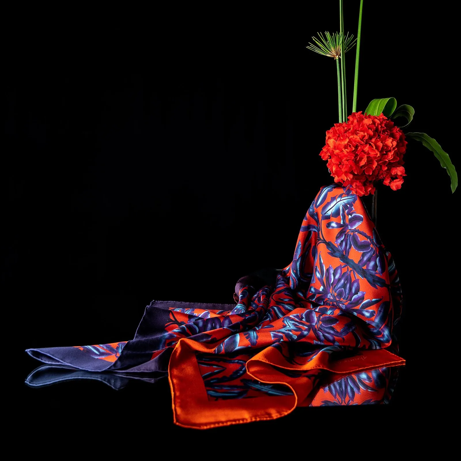 Aubrey Kurlansky's Blue Dragons on Vermilion Ground silk scarf draped beneath a red flower, on black