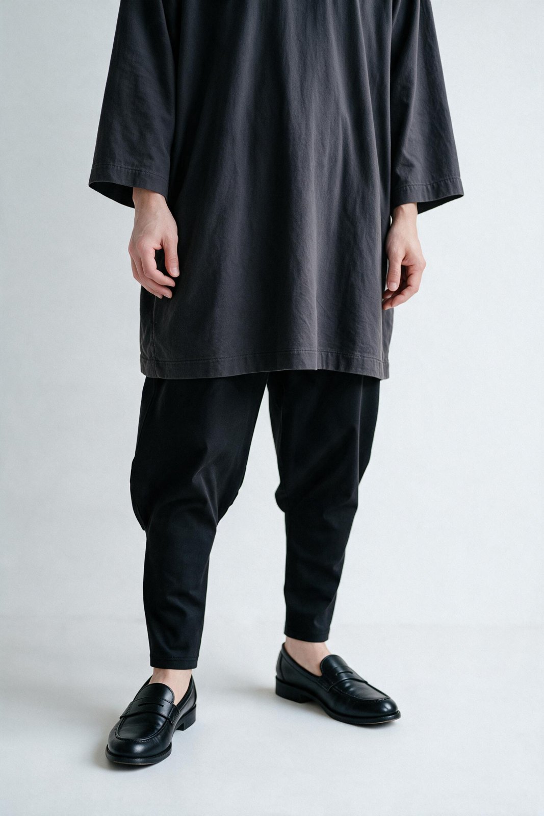 Front view of black Kanso Cut pants under a long charcoal tunic: full through the thigh, a smooth step at the knee and a long slim lower leg, with black loafers